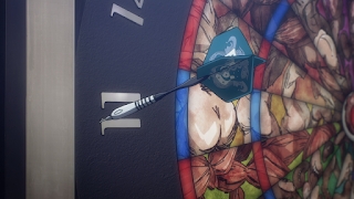 A dart is embedded in a dartboard featuring colorful, abstract designs in this anime still.